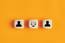 Wooden blocks with people icons are on either side of scale of law icon block. The blocks are on an orange background 